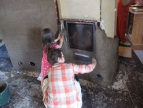 Uunin päällystämistä cob-tekniikalla, savi-olki-hiekka-vesikerroksella. Puhtaalla savella  rakentamiseen voi lapsetkin vaaratta osallistua.